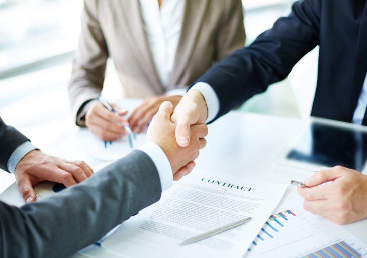 Image of business partners handshaking over business objects on workplace